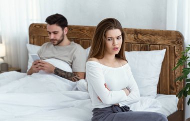 Tartışma ve kıskançlık. Yatakta akıllı telefondan konuşan, incinmiş bir kız kollarını kavuşturmuş.