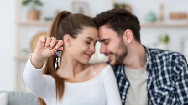 Första hem för ung familj. Lycklig man och hustru i vardagsrummet, kvinna visar nycklar — Stockfoto