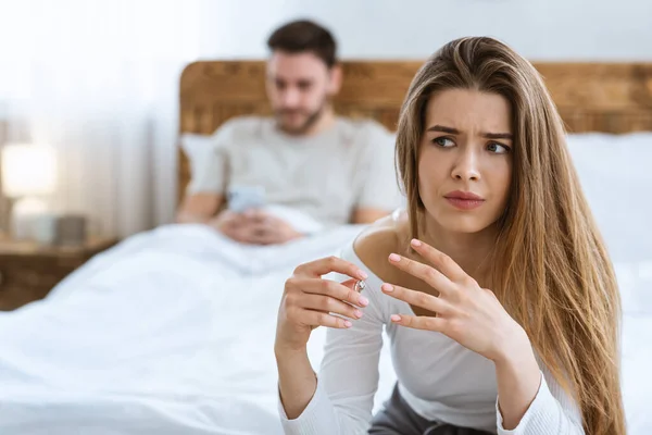 Triste esposa se quita su anillo de bodas de cerca, marido escribiendo en el teléfono en la cama —  Fotos de Stock