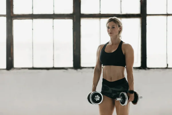 Спортивная женщина в спортивной одежде с умными часами занимается фитнесом с гантелями в тренажерном зале — стоковое фото