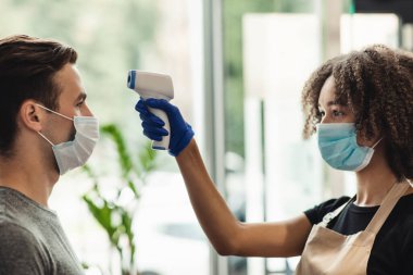 İşlemlerden önce müşterinin vücut ısısını ölçen kadın berber