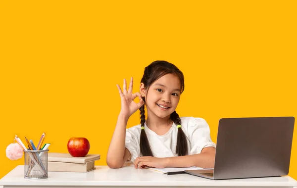 Escuela coreana chica gestos bien sentado en el escritorio, fondo amarillo —  Fotos de Stock