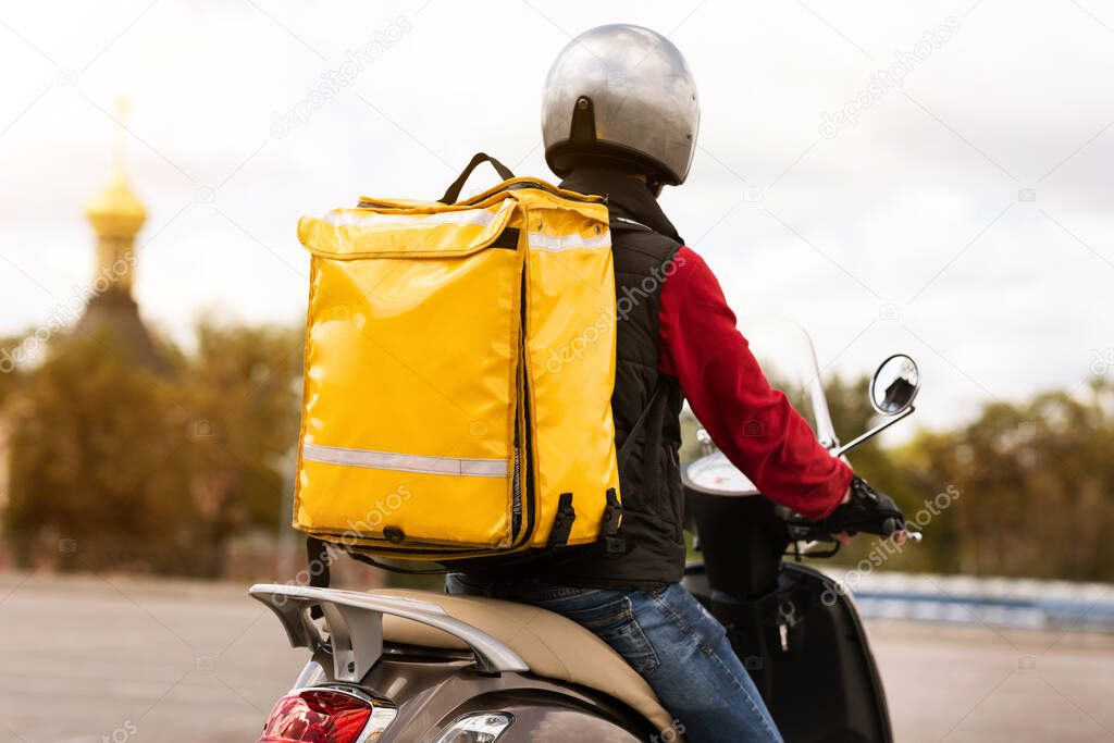 Courier With Yellow Backpack Delivering Meals On Scooter Outside, Rear-View