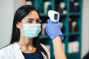 Güzellik salonuna girerken vücut ısısını kontrol eden genç kadınlar.