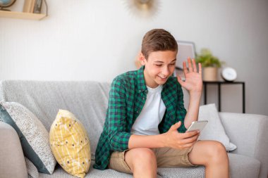 Evde telefon kullanan, videolu görüşme yapan pozitif bir genç.
