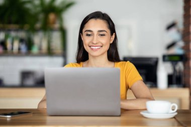 Cafe 'de oturup dizüstü bilgisayar kullanan neşeli Arap kız öğrenci.