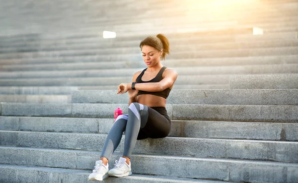 Atlética mujer negra sentada en las escaleras, comprobando en smartwatch — Foto de Stock