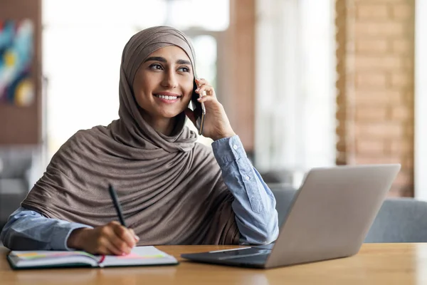 Femme musulmane pigiste parlant au client au téléphone, prenant des notes — Photo