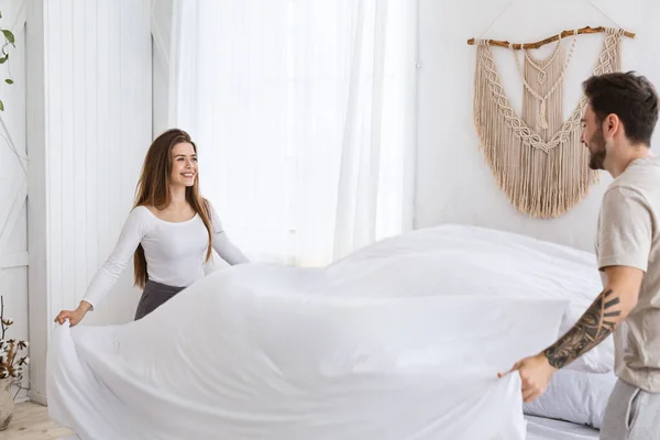 Clean up in bedroom. Smiling young man and woman making bed in morning — Stock Photo, Image