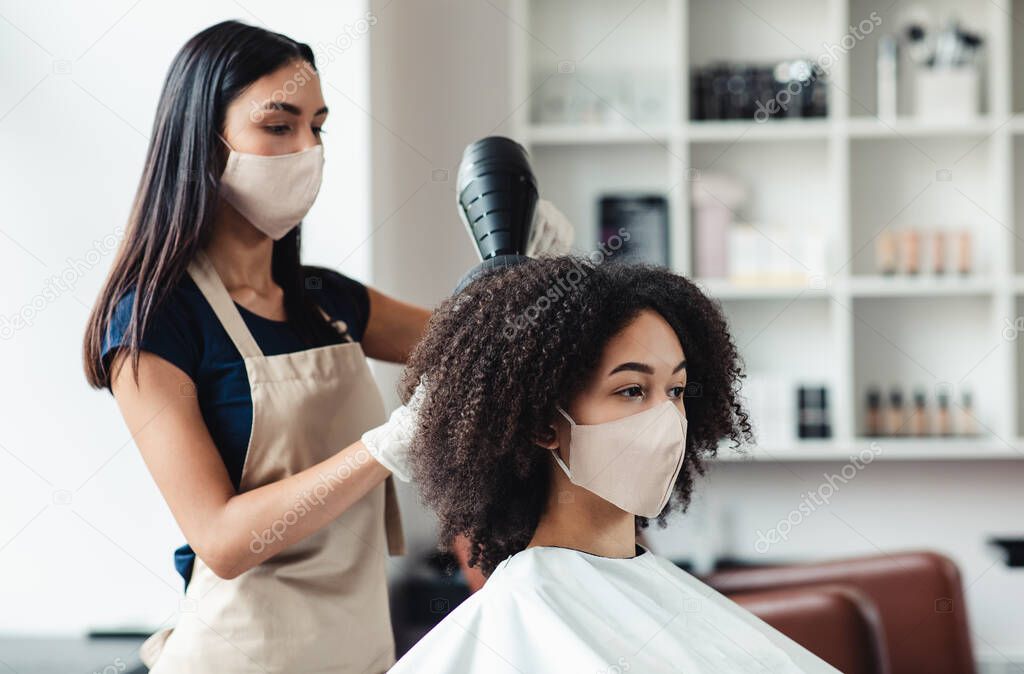 Hairdresser and customer wearing protective masks at beauty salon