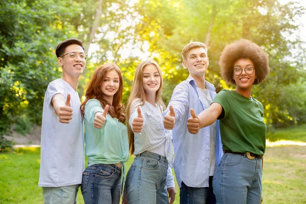 Groep van multi-etnische tiener vrienden staan buiten toont duimen omhoog bij de camera — Stockfoto