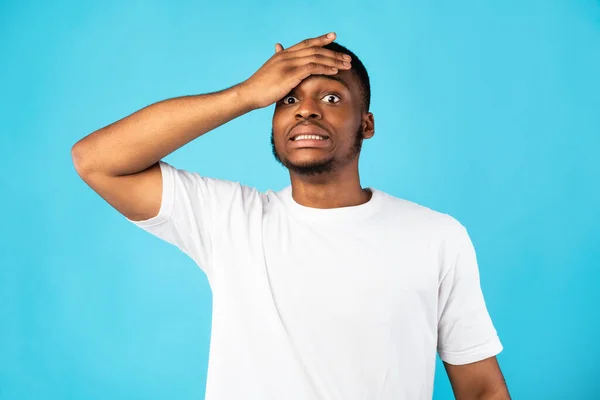 Verwirrter afroamerikanischer Guy, der den Kopf über blauem Hintergrund berührt — Stockfoto
