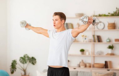 Evde dayanıklılık eğitimi. Oturma odasında pazılar üzerinde çalışan güçlü bir adam.