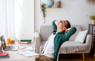 Uykucu öğrenci dizüstü bilgisayarın önünde oturuyor ve esniyor.