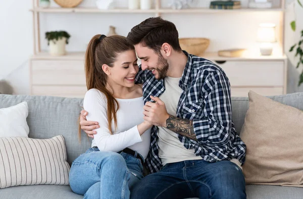 Glad tillsammans hemma. Glad ung man och kvinna i avslappnade kläder håller hand, kramas på soffan — Stockfoto