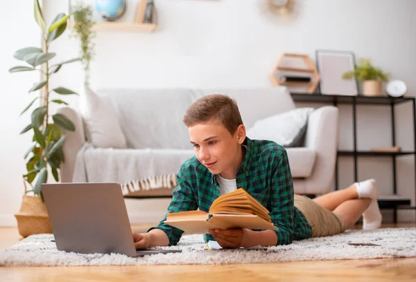 Fröhlicher Teenager liest Buch und tippt auf Laptop — Stockfoto