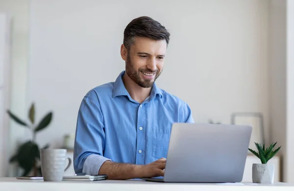 Schöner männlicher Unternehmer arbeitet am Laptop am Schreibtisch im modernen Büro — Stockfoto