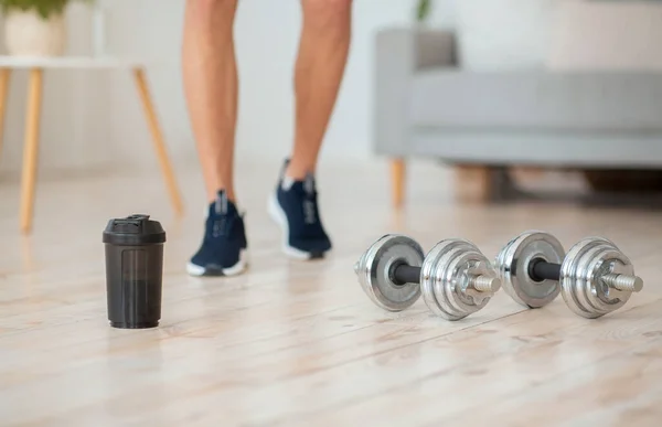 Guy in sneakers goes to dumbbells and glass of protein shake on wooden floor — Stock Photo, Image