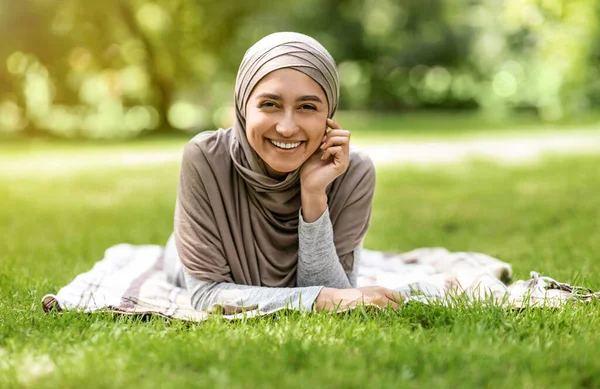 Chica árabe alegre en hijab acostado en la hierba en el parque —  Fotos de Stock