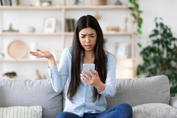 Gefrustreerd aziatisch meisje zitten met smartphone op de bank, emotioneel reageren op bericht — Stockfoto