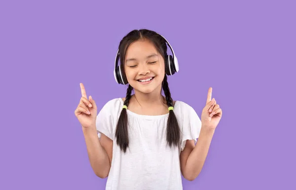 Menina em fones de ouvido gostando de ouvir música, fundo roxo — Fotografia de Stock