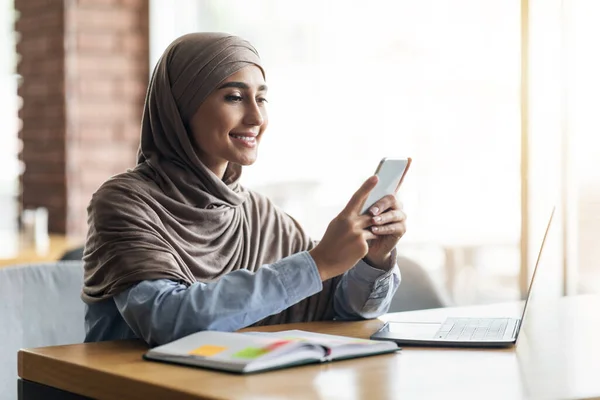 Fiatal nő hidzsáb laptoppal okostelefon a kávézóban — Stock Fotó