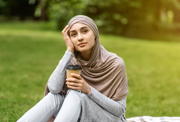 Chica árabe soñadora sentada sola en el parque, bebiendo café —  Fotos de Stock