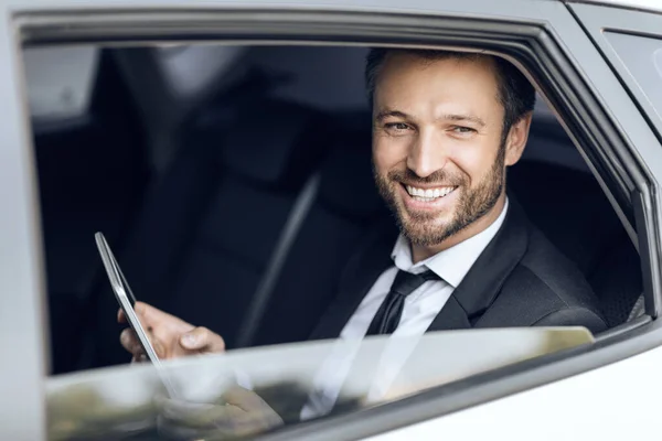 Улыбающийся красивый бизнесмен в костюме сидит в машине — стоковое фото
