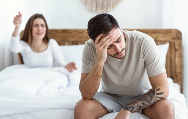 Müde von Skandalen. Junge Frau schwört, trauriger Mann hält Kopf mit Hand und sitzt auf Bett — Stockfoto