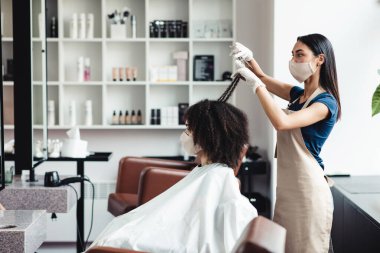 Koruyucu maskeli genç siyah kız kuaförlerde saç tıraşı oluyor.