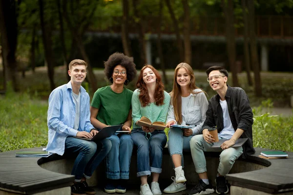 Grupo de estudiantes de secundaria multiraciales felices sentados juntos en el banco en el parque —  Fotos de Stock