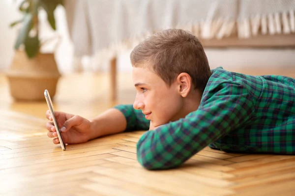 Счастливый подросток пользуется мобильным телефоном, лежа на полу дома — стоковое фото
