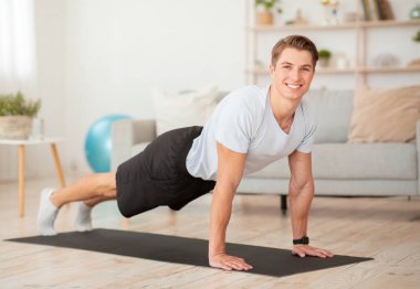 Formda kal ve evde egzersiz yap. Gülümseyen kaslı adam iç mekanda şınav çekiyor.