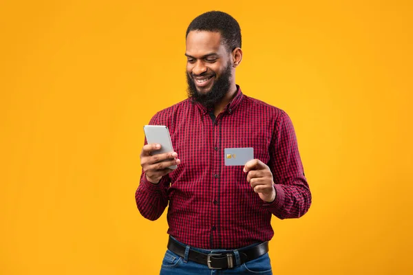 Preto masculino segurando cartão de crédito e celular no estúdio — Fotografia de Stock