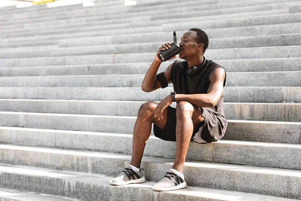 Thursty Negro Hombre Atleta Agua Potable, Descanso en las escaleras urbanas después de entrenar al aire libre —  Fotos de Stock