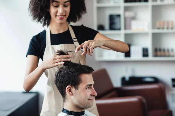 African american hairdresser cutting hair for young man at barber shop — Stock Photo, Image