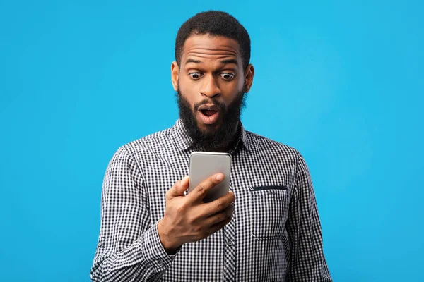 Sorprendido hombre afro utilizando el teléfono móvil en la pared azul — Foto de Stock