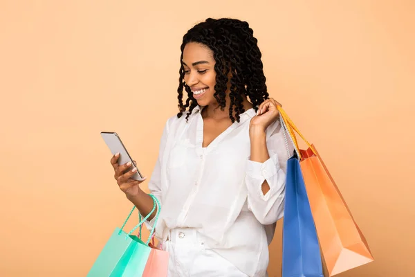 Felice africano ragazza utilizzando cellulare holding shopper borse, studio girato — Foto Stock