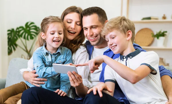 Rodiče a děti pomocí mobilního telefonu sedí na gauči doma — Stock fotografie