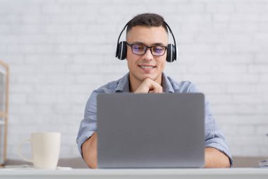 Salgın sırasında evde online dersler. Kulaklıklı adam masada oturur ve dizüstü bilgisayarına bakar.