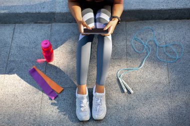 Sportif kadın telefon kullanıyor, açık hava eğitiminden sonra dinleniyor.