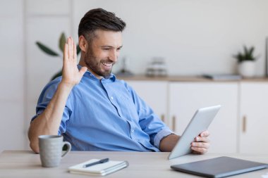 Ofisinde dijital tabletle ailesine video görüşmesi yapan neşeli iş adamı.