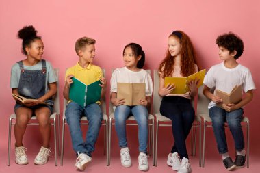 Sandalyelerin üzerinde çalışma materyalleri olan çok ırklı şirin öğrenciler.