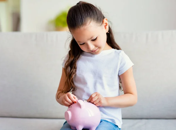 Niña poniendo monedas en Piggybank con ahorros en casa — Foto de Stock