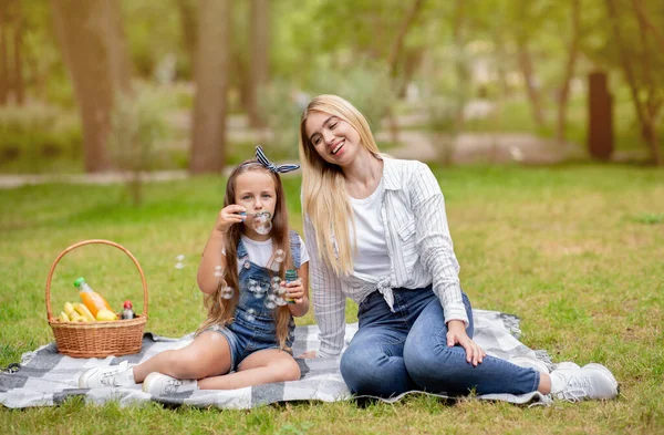 Flicka och hennes mor blåser bubblor ha kul i parken — Stockfoto