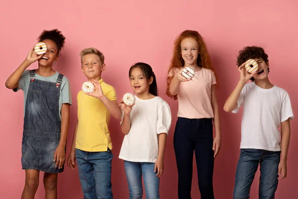 具有粉色背景的美味甜甜圈的快乐的多种族学童 — 图库照片