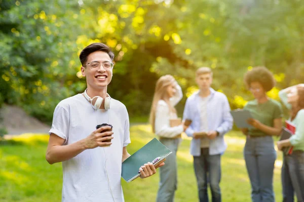 Porträt eines lächelnden asiatischen männlichen Studenten, der mit Arbeitsbüchern und Kaffee im Freien posiert — Stockfoto