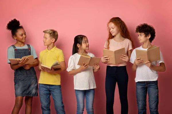 Retrato de niñas y niños lindos con libros de texto de la escuela mirándose unos a otros sobre fondo rosa —  Fotos de Stock