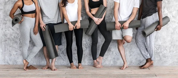 Diversas personas en ropa deportiva con colchonetas de yoga en las manos posando cerca de la pared — Foto de Stock