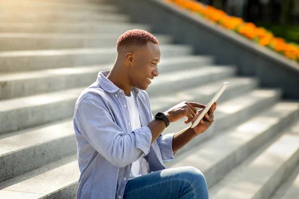 Millennial μαύρο άνδρα περιήγηση στο διαδίκτυο στον υπολογιστή tablet, ενώ κάθεται σε σκάλες έξω — Φωτογραφία Αρχείου